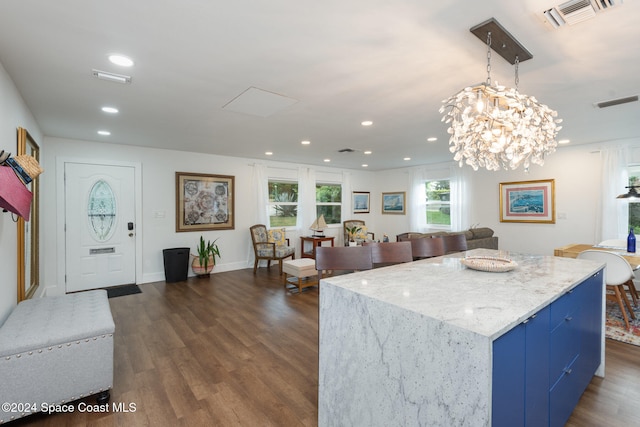 kitchen with a center island, an inviting chandelier, blue cabinets, dark hardwood / wood-style floors, and light stone counters