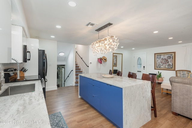 kitchen with a center island, hanging light fixtures, light hardwood / wood-style flooring, blue cabinets, and a breakfast bar