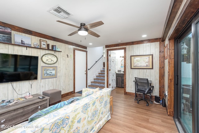 living room with light hardwood / wood-style floors, ceiling fan, and wood walls