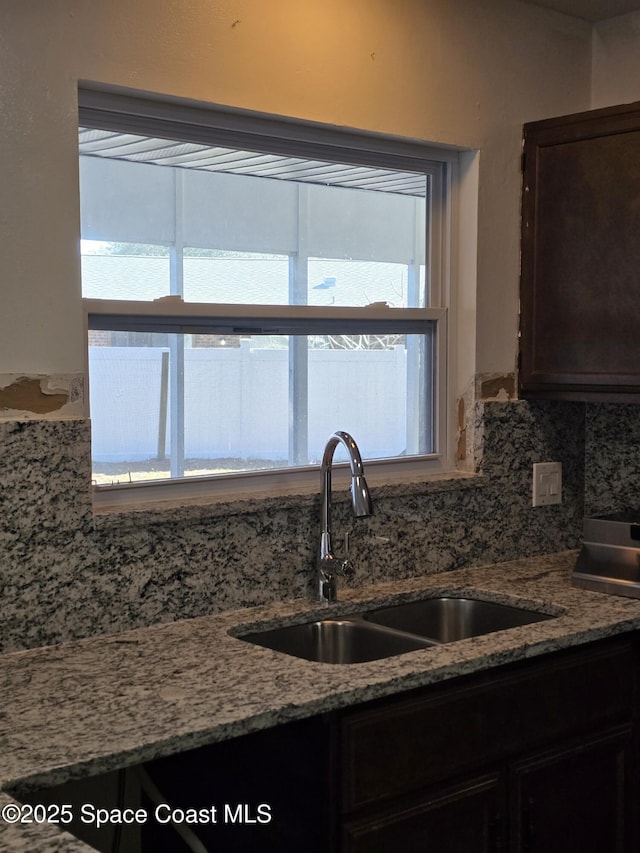 kitchen with tasteful backsplash, dark brown cabinets, sink, and light stone counters