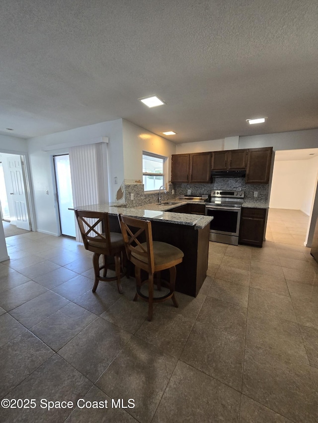 kitchen with a breakfast bar, sink, stainless steel range with electric stovetop, dark brown cabinetry, and kitchen peninsula