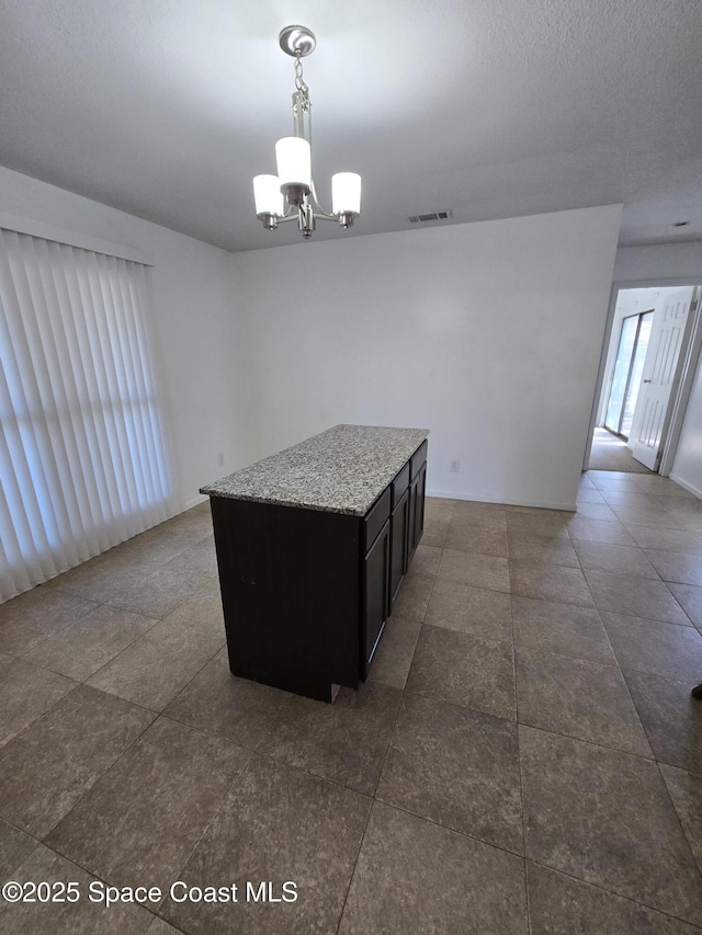 kitchen featuring pendant lighting, light stone countertops, a kitchen island, and a notable chandelier