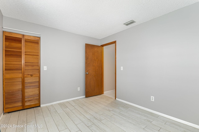 unfurnished bedroom with a closet, a textured ceiling, and light wood-type flooring