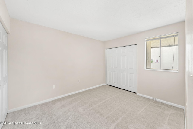 unfurnished bedroom with light colored carpet and a closet