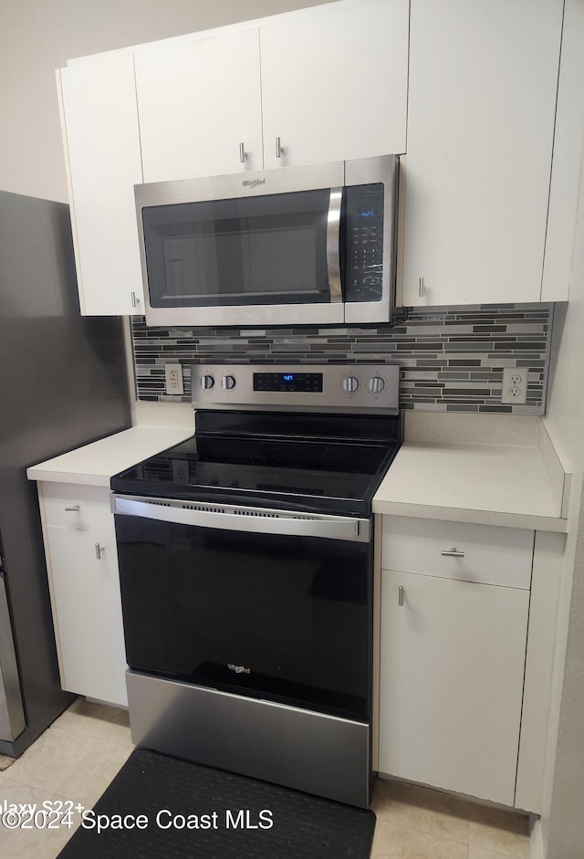 kitchen featuring decorative backsplash, white cabinets, light tile patterned floors, and appliances with stainless steel finishes