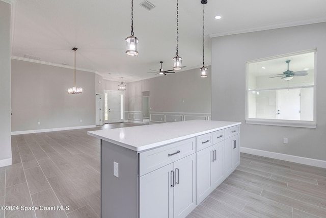 kitchen featuring crown molding, decorative light fixtures, light hardwood / wood-style flooring, white cabinets, and a center island