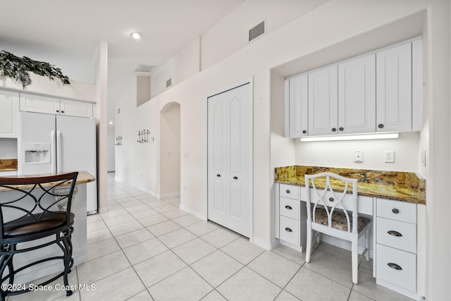 kitchen featuring white fridge with ice dispenser, white cabinetry, light tile patterned floors, and dark stone counters