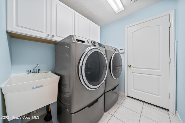 clothes washing area featuring cabinets, sink, light tile patterned floors, a textured ceiling, and washing machine and clothes dryer