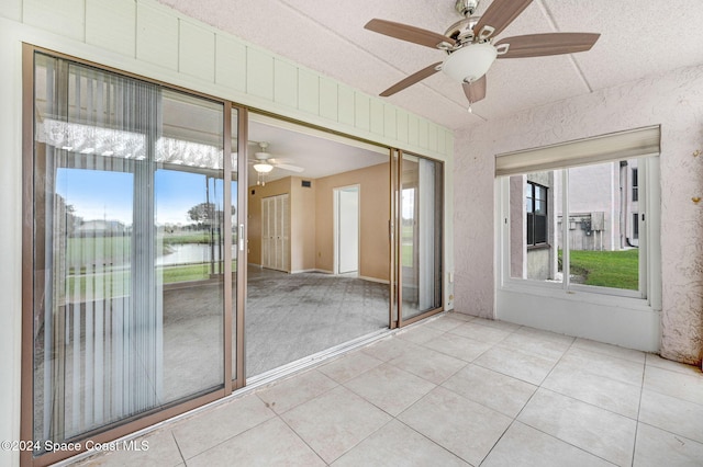 unfurnished sunroom featuring ceiling fan, a water view, and a healthy amount of sunlight