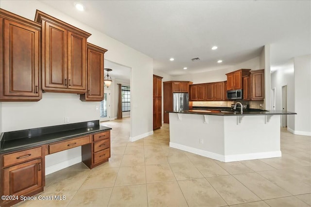 kitchen with a kitchen bar, an island with sink, light tile patterned floors, and appliances with stainless steel finishes