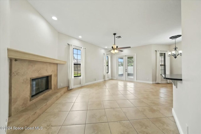 unfurnished living room with french doors, ceiling fan with notable chandelier, plenty of natural light, and a tiled fireplace