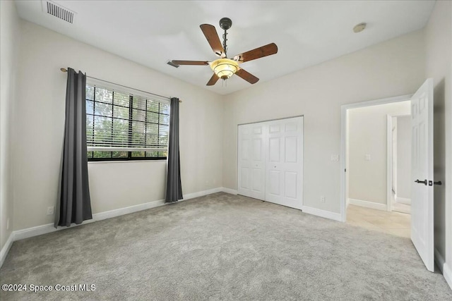 unfurnished bedroom with a closet, light colored carpet, and ceiling fan