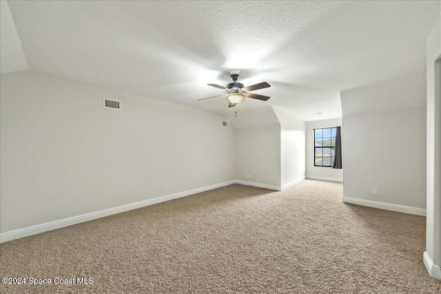 carpeted spare room featuring a textured ceiling, vaulted ceiling, and ceiling fan