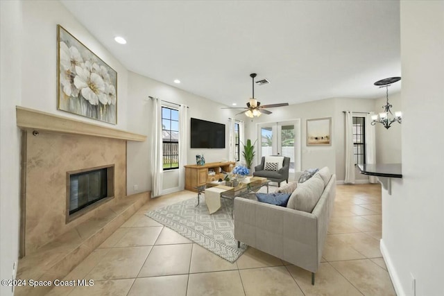 tiled living room with a tiled fireplace, a healthy amount of sunlight, and ceiling fan with notable chandelier