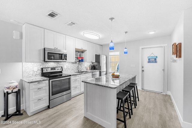 kitchen featuring pendant lighting, white cabinets, light hardwood / wood-style flooring, appliances with stainless steel finishes, and light stone counters