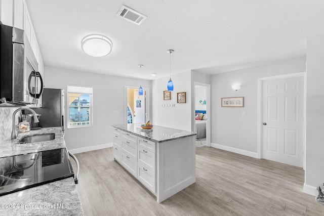 kitchen featuring pendant lighting, light hardwood / wood-style floors, white cabinetry, and light stone counters