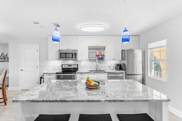 kitchen with pendant lighting, white cabinets, sink, light stone counters, and stainless steel appliances