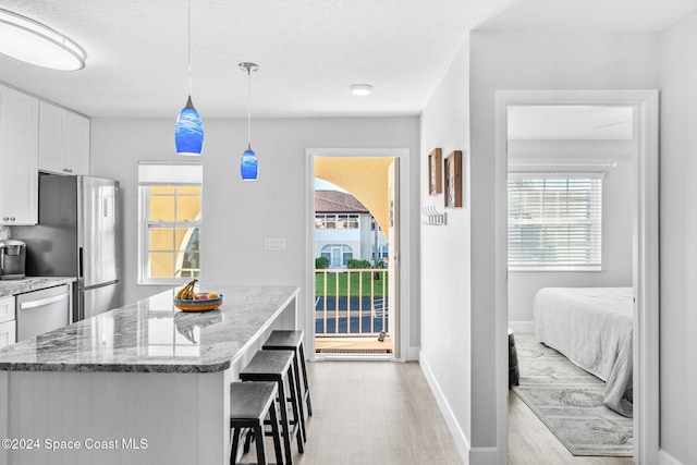 kitchen with white cabinetry, light hardwood / wood-style floors, a textured ceiling, decorative light fixtures, and appliances with stainless steel finishes