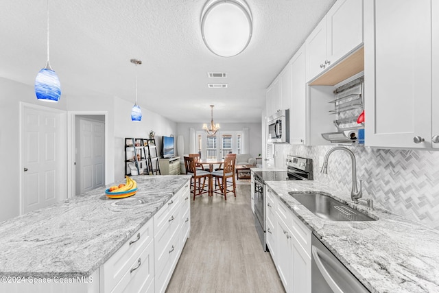 kitchen with sink, appliances with stainless steel finishes, pendant lighting, white cabinets, and light wood-type flooring