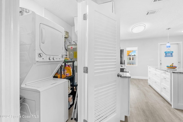 laundry room with a textured ceiling, light wood-type flooring, and stacked washer and clothes dryer