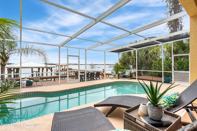 view of swimming pool with glass enclosure, a patio area, and a water view