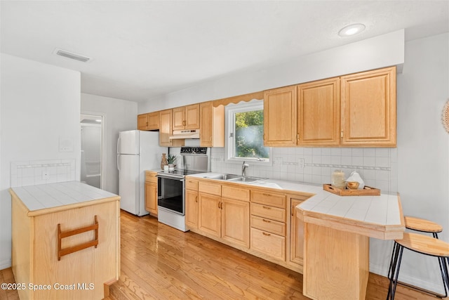 kitchen with tile countertops, a breakfast bar, light brown cabinetry, and white appliances