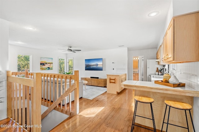 kitchen featuring backsplash, kitchen peninsula, light brown cabinetry, and a kitchen breakfast bar