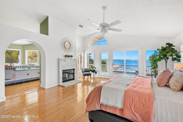 bedroom featuring access to exterior, ceiling fan, a water view, lofted ceiling, and a tiled fireplace