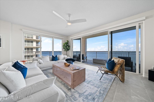 living room featuring ceiling fan, a water view, and a textured ceiling