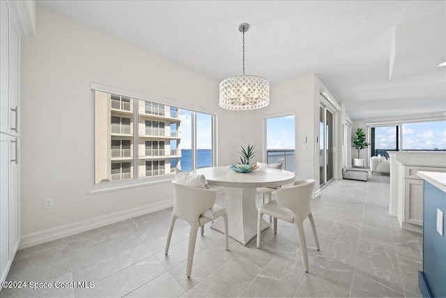 dining space with a water view, a textured ceiling, a wealth of natural light, and an inviting chandelier