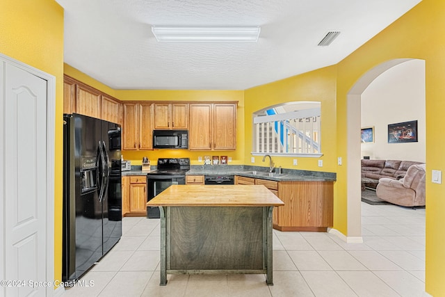 kitchen featuring light tile patterned floors, a textured ceiling, a kitchen island, black appliances, and sink