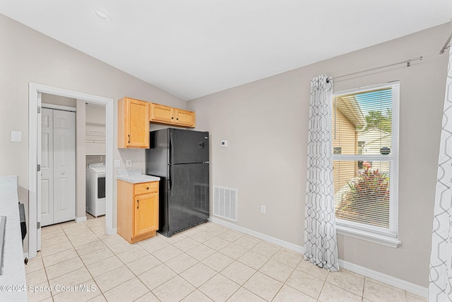 kitchen featuring vaulted ceiling, washer / dryer, black refrigerator, light brown cabinetry, and light tile patterned flooring