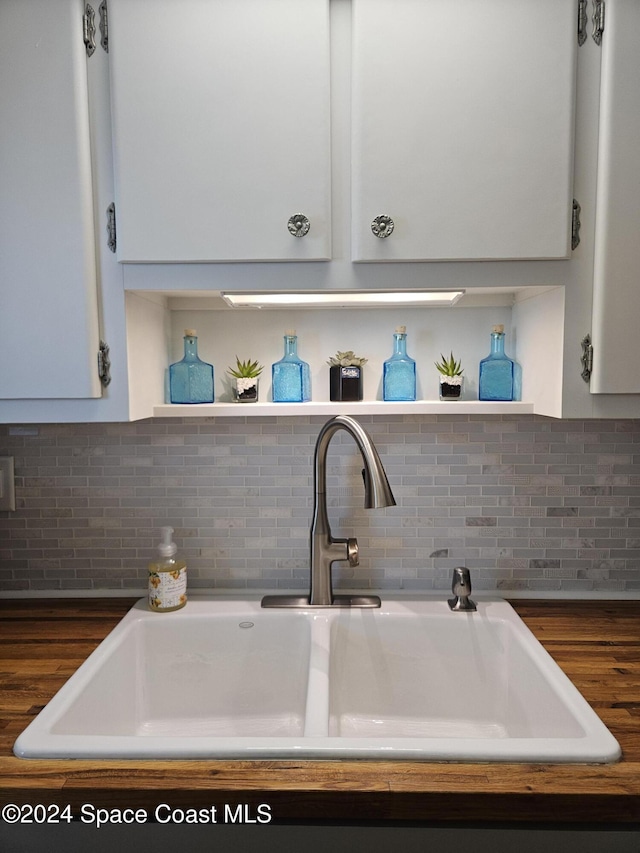 room details with tasteful backsplash, white cabinetry, and sink