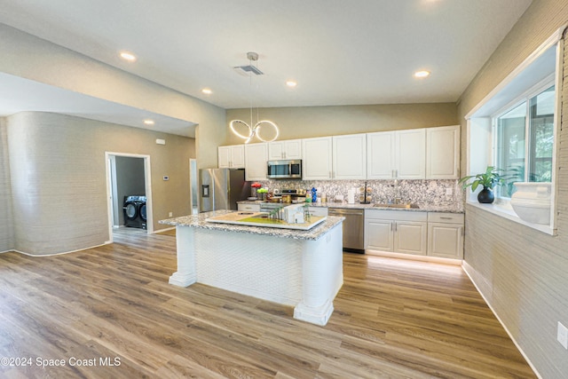 kitchen featuring a center island, vaulted ceiling, decorative backsplash, appliances with stainless steel finishes, and white cabinetry