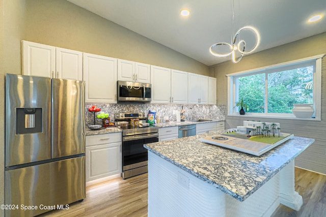 kitchen with light stone countertops, stainless steel appliances, vaulted ceiling, pendant lighting, and white cabinets