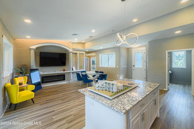 kitchen featuring decorative light fixtures, a kitchen island, light stone countertops, and light hardwood / wood-style floors