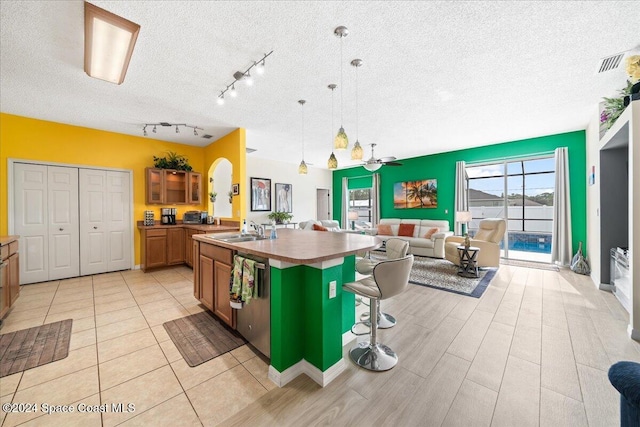 kitchen featuring pendant lighting, dishwasher, a breakfast bar, an island with sink, and a textured ceiling