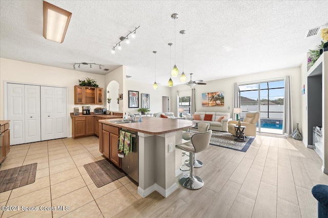 kitchen featuring a breakfast bar, a kitchen island with sink, stainless steel dishwasher, a textured ceiling, and decorative light fixtures