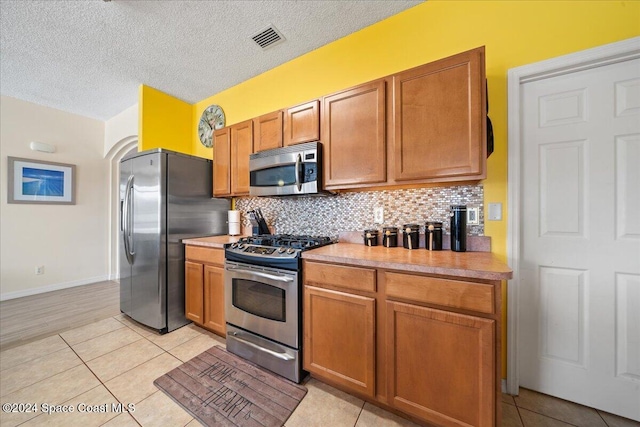 kitchen with backsplash, light tile patterned flooring, stainless steel appliances, and a textured ceiling