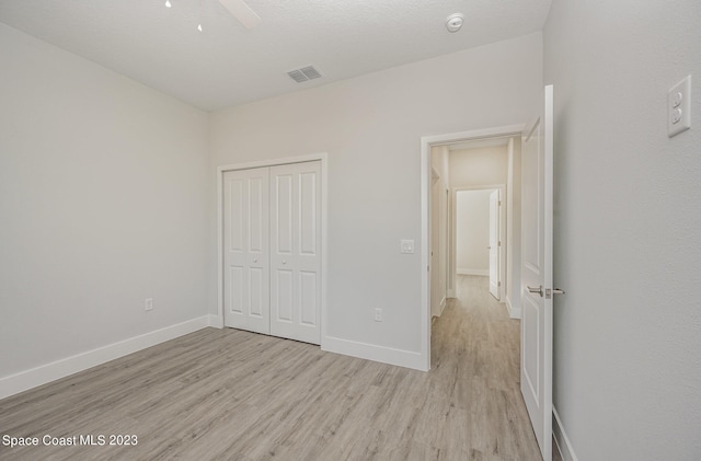 unfurnished bedroom with a textured ceiling, light hardwood / wood-style flooring, a closet, and ceiling fan