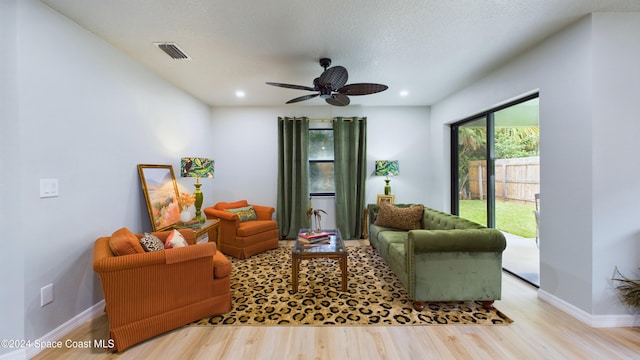 living area featuring ceiling fan, light wood-type flooring, and a textured ceiling