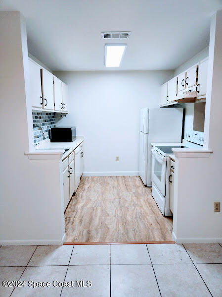 kitchen with white electric stove, light tile patterned floors, visible vents, and under cabinet range hood