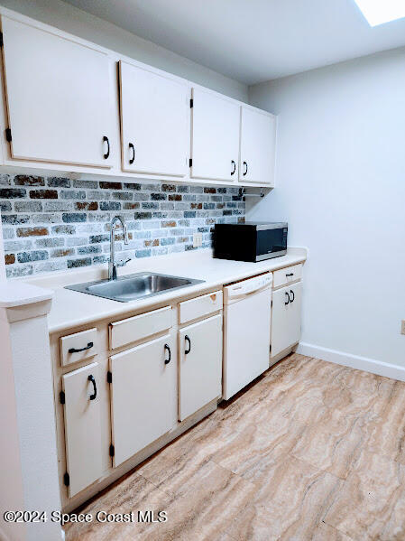 kitchen with a sink, white cabinets, dishwasher, and light countertops