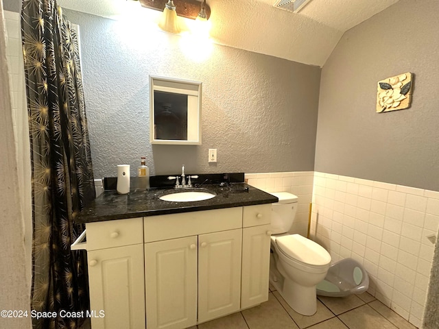 bathroom with tile patterned floors, vanity, a textured ceiling, tile walls, and toilet