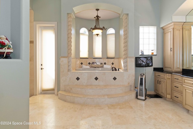 bathroom with vanity, a high ceiling, tiled tub, and a chandelier