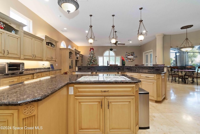 kitchen with dark stone countertops, a kitchen island, sink, and hanging light fixtures