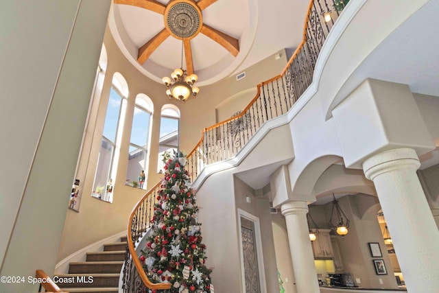 staircase with ornate columns, a chandelier, and a high ceiling