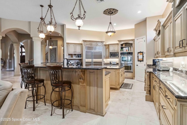 kitchen featuring arched walkways, decorative columns, a spacious island, built in appliances, and a kitchen breakfast bar