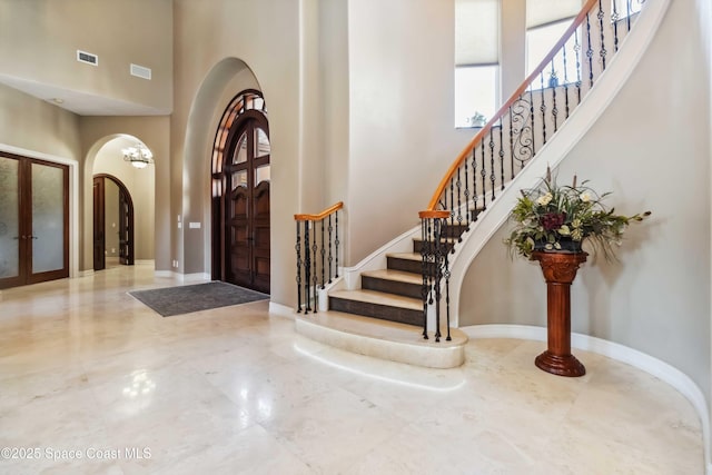 foyer entrance featuring arched walkways, a high ceiling, stairway, and visible vents