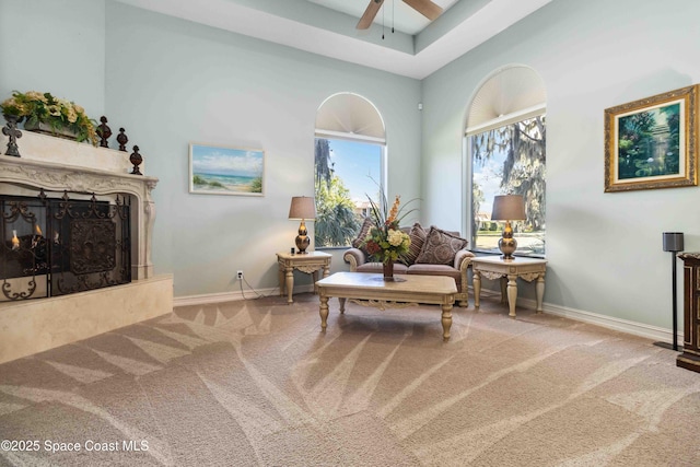 sitting room with a ceiling fan, a high end fireplace, carpet flooring, and baseboards